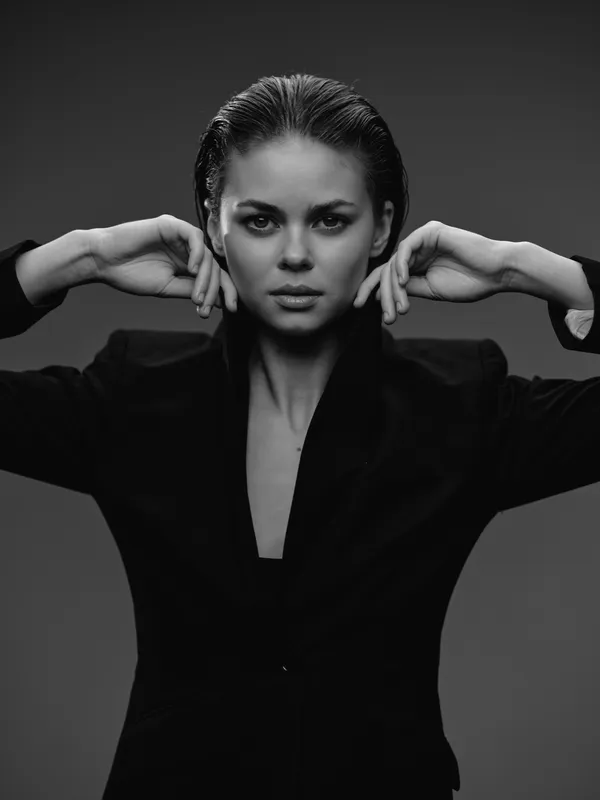 Black and white portrait of confident woman in blazer with slicked-back hair in studio lighting.
