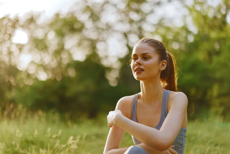Young athletic woman enjoying nature in a green field, wearing sportswear, with a calm and relaxed expression, epitomizing fitness and well being in summer