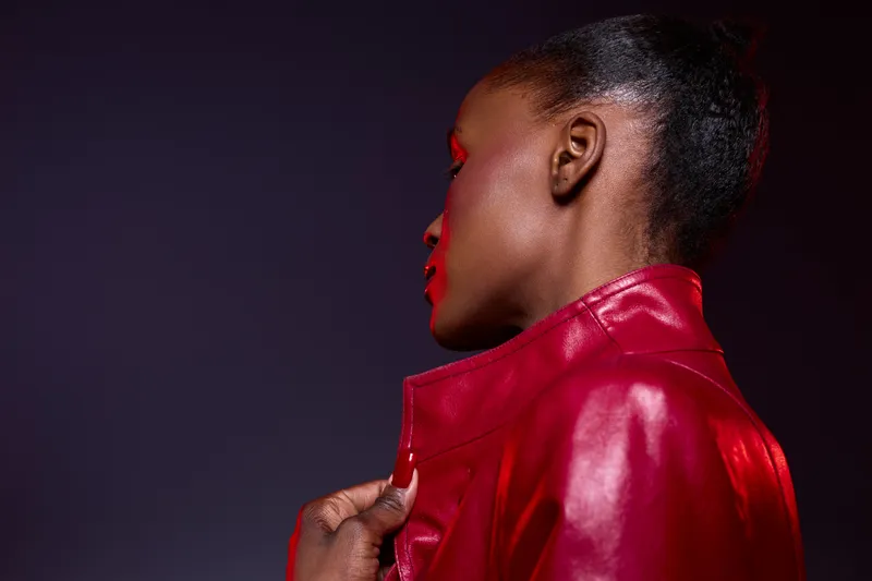 Profile of a young African woman with dark skin wearing a red leather jacket against dark background. Concept of fashion, style, confidence, and modern beauty portrait.