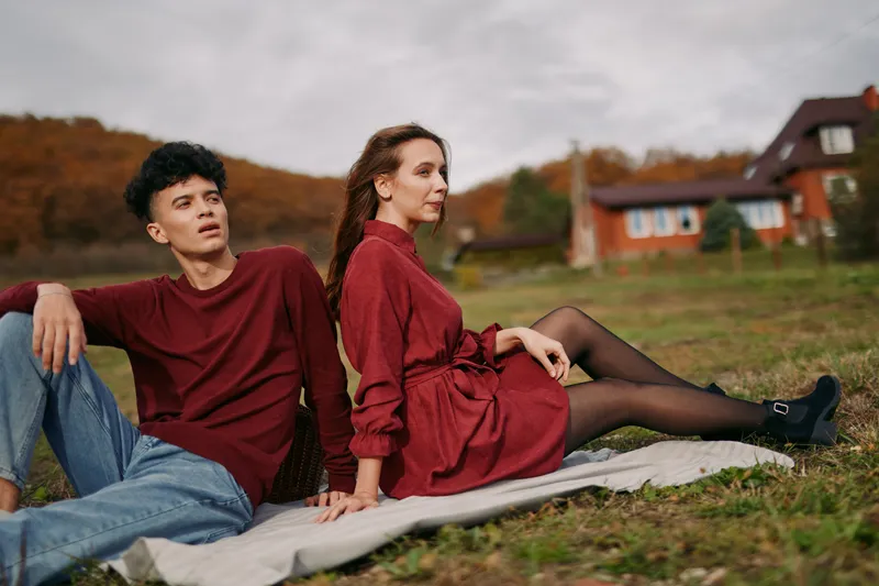Young couple relaxing on a picnic blanket in the countryside, sharing an authentic, candid moment in coordinated autumn outfits, conveying genuine connection and credible emotional presence.