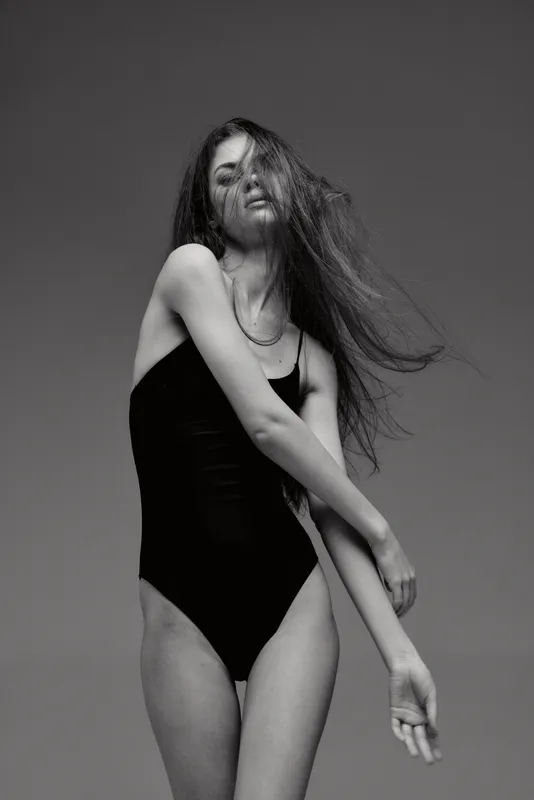 Black and white portrait of a young woman in a black swimsuit with flowing hair and a graceful pose.