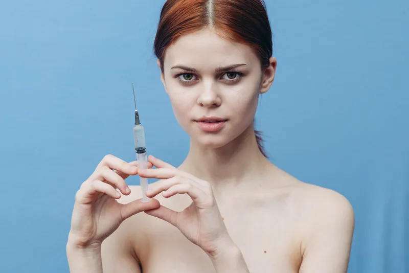 Женщина делает инъекцию, обнаженные плечи, испуганное лицо на синем фоне