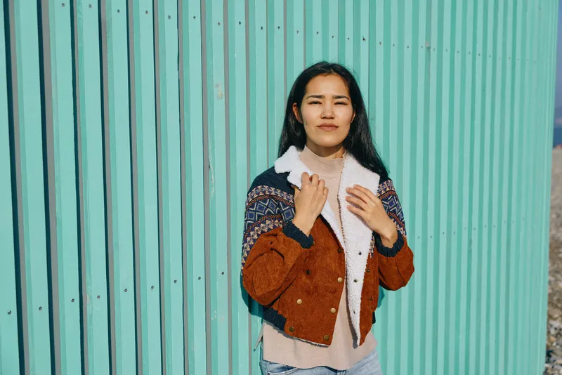 Fashion, woman wearing a textured brown jacket against a vibrant teal wall, casual chic style for streetwear mood, confident pose and contemporary vibe in outdoor setting