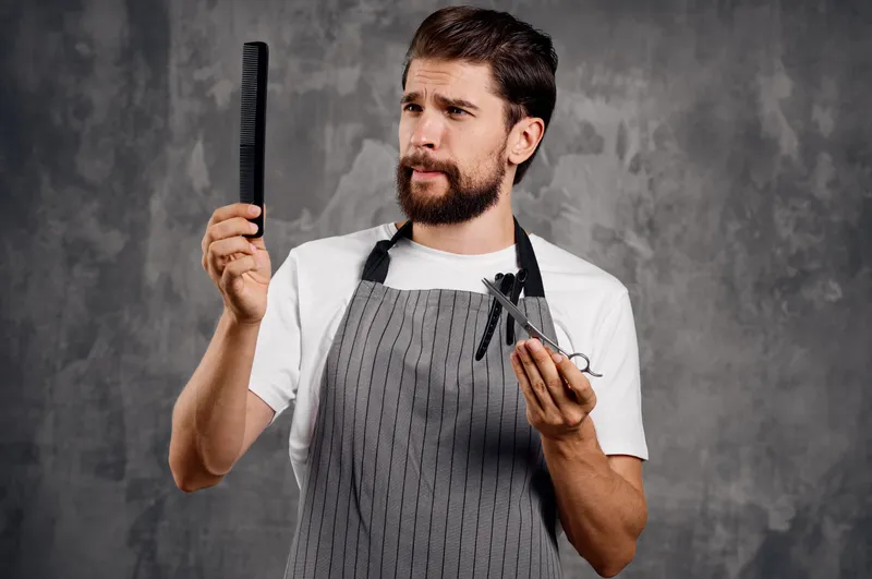 Бородатый мужчина держит в руке ножницы и расчёску, парикмахер, укладка волос, барбершоп
