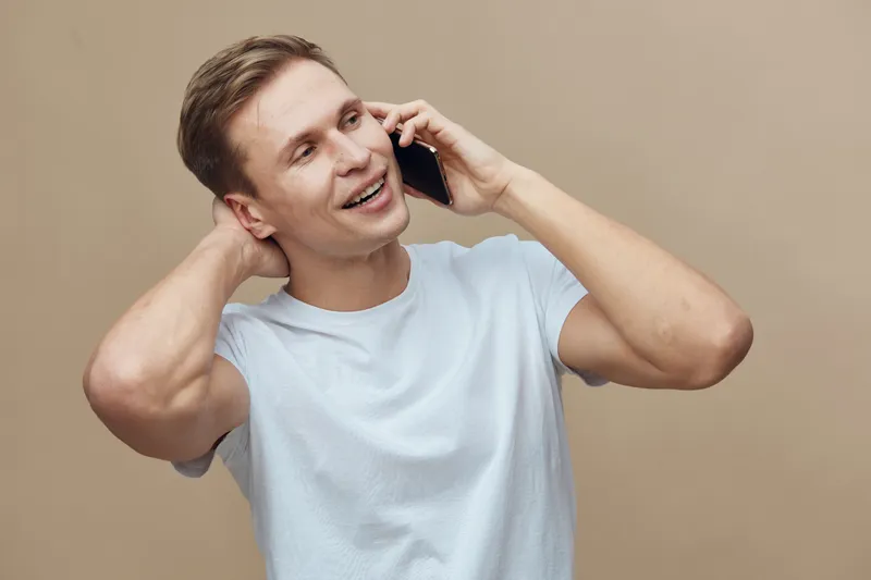 smiling man talking on phone casual white tshirt beige background happy communication digital nomad concept