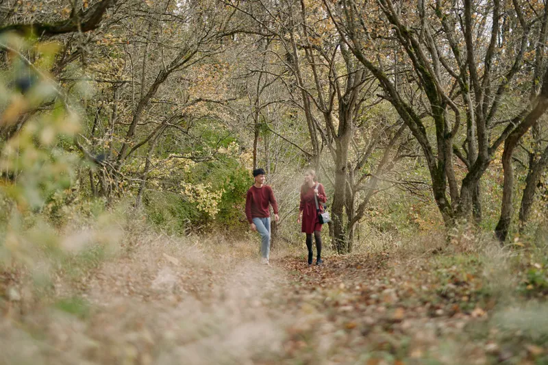 A genuine candid portrait of a couple walking through an autumn woodland path, conveying authentic connection, natural light, and quiet everyday moments of trust and togetherness.