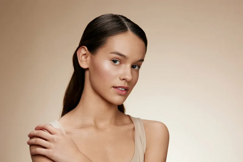 Young woman with smooth skin and natural makeup, posing gracefully against a soft beige background, evoking a sense of calm and beauty