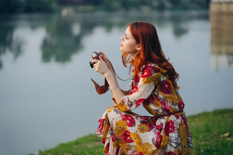Рыжеволосая женщина с фотоаппаратом на природе у озера