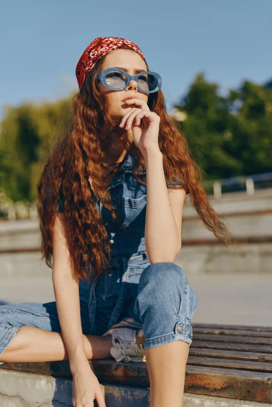 Lifestyle woman in modern boho-western denim street style wearing blue sunglasses and red bandana, embodying relaxed summer fashion with film color tones.