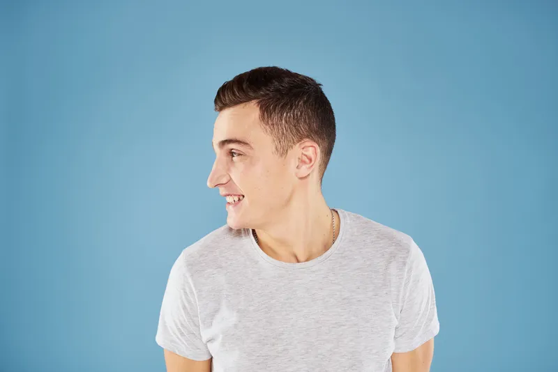 Эмоциональный мужчина в белой футболке, кадрированный вид на синем фоне