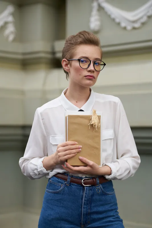 Красивая студентка с книгой в руке возле здания, модель в костюме, кадрированный вид