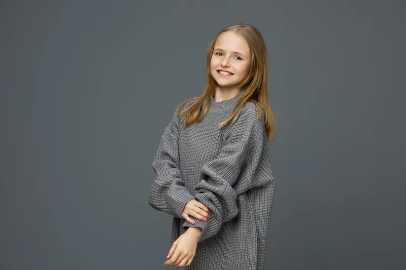 Smiling girl in a cozy gray sweater against a gray background, showcasing comfort and warmth in a minimalistic style perfect for seasonal fashion trends