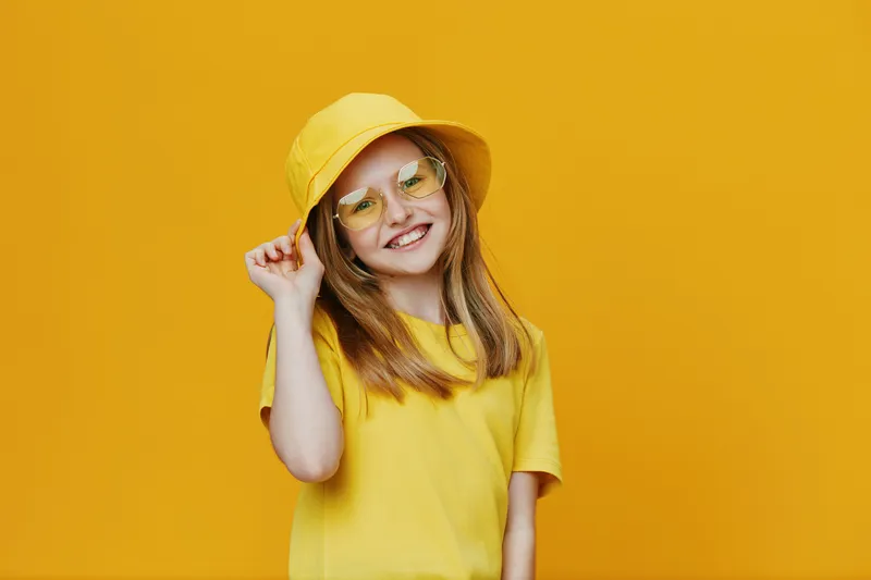 Cheerful girl in yellow attire with sunglasses, posing against a bright yellow background, embodying joy and summer vibes for playful portrait photography