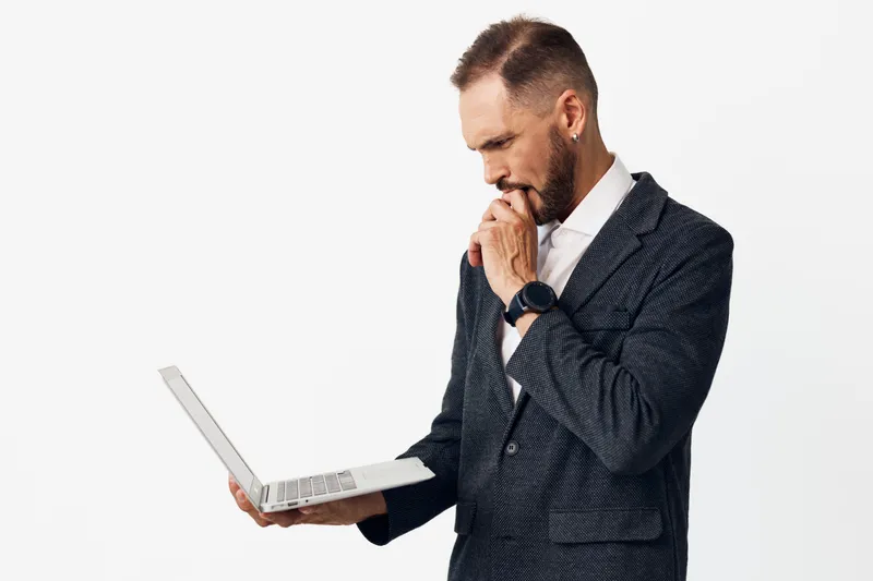 A professional businessman stands with a laptop, looking thoughtful on an isolated colored backdrop, conveying focus, confidence, and determination in a corporate, modern setting.
