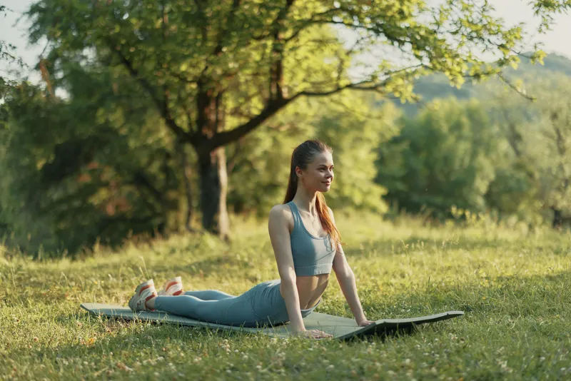 Young woman practicing yoga outdoors in a serene environment, wearing comfortable athletic wear, embodying health and tranquility, with a lush green background