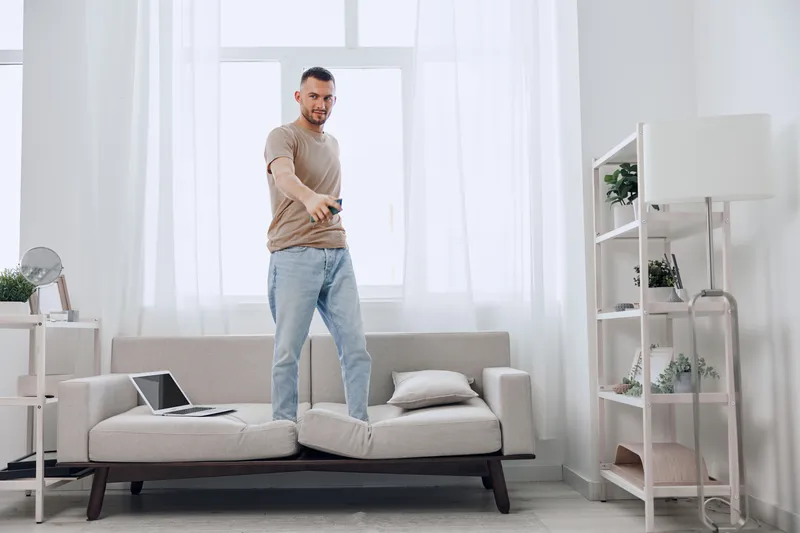Motivated man standing on couch, smiling confidently in a bright, modern living room. Warm colors create an inviting atmosphere for home inspiration.