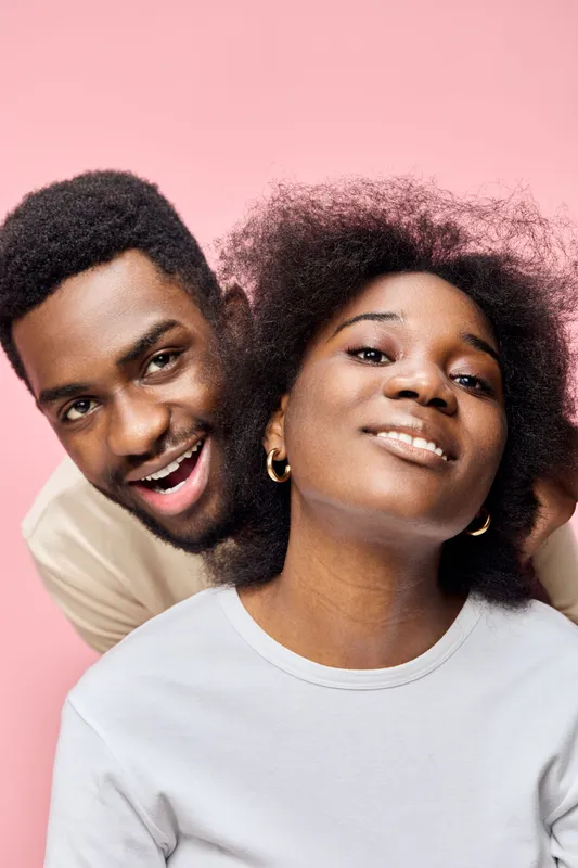 Happy young couple with natural hair, smiling on a pink background, showcasing love and joy in a playful and intimate moment
