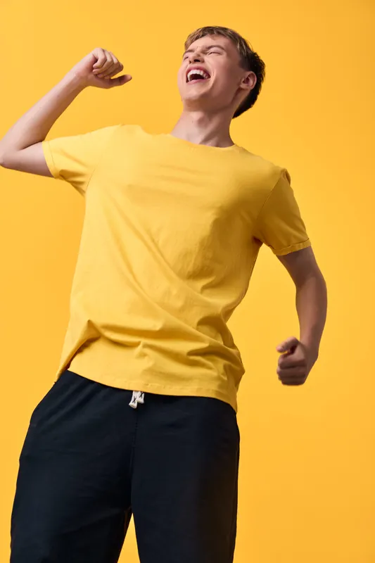 Joyful man in a yellow tee pumps his fist in celebration, bright orange background, energetic mood, expressive movement, dynamic sportswear vibe, for stock use and lifestyle context