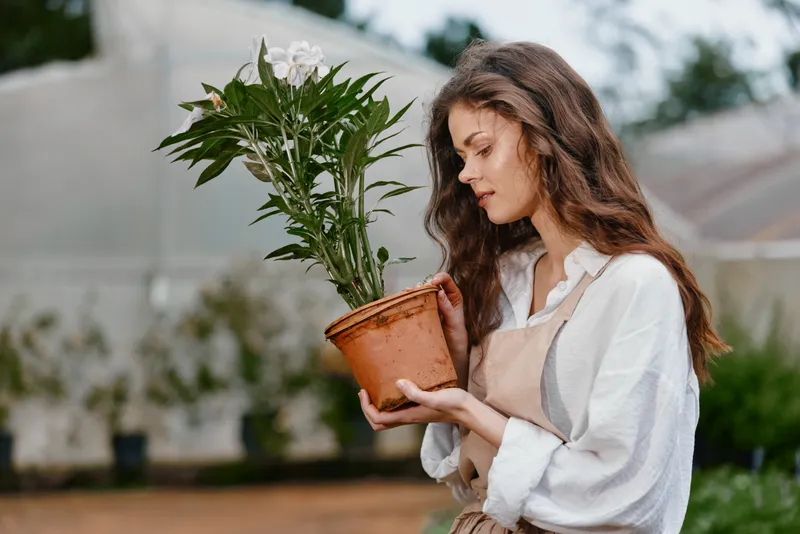 Young woman in natural setting nurturing a potted plant, showcasing emotions of joy and care, perfect for concepts related to gardening and sustainable living