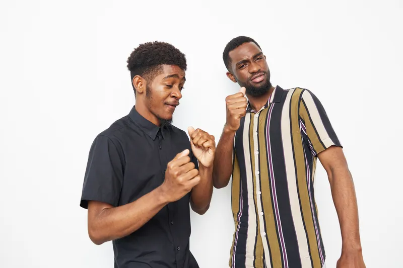 Two joyful Black men dancing together, celebrating friendship with playful expressions and vibrant outfits, showcasing happiness and connection in a dynamic setting.