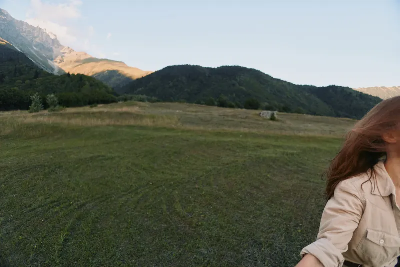 Woman lifestyle in an open field with distant mountains, natural landscape, casual beige jacket, feeling of freedom and outdoor exploration under a sunny sky