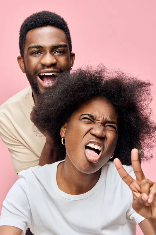 Happy African American couple having fun on a pink background, showing playful emotions with vibrant colors and casual clothing