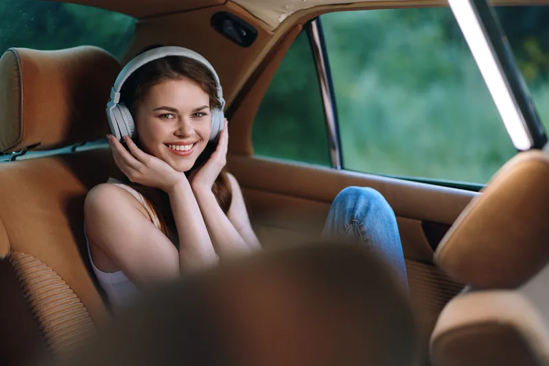 Young woman enjoying music with headphones in a cozy car, exuding joy and relaxation with a soft, natural background and warm colors.