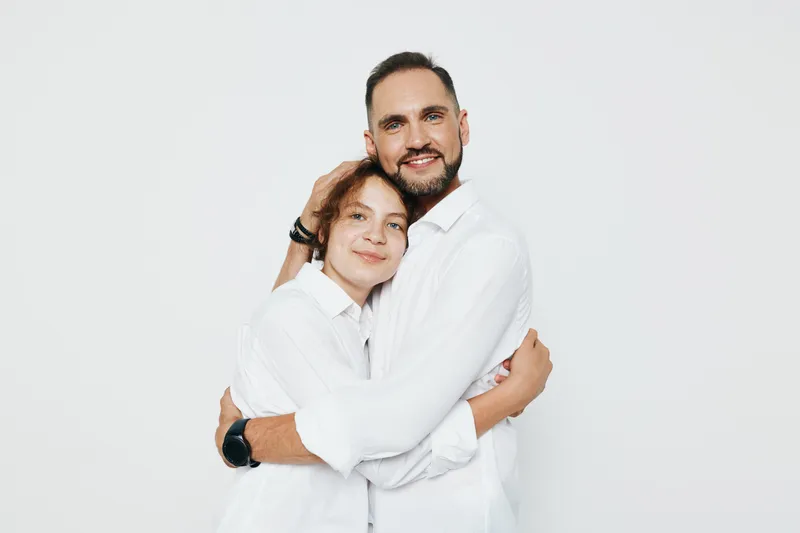A professional man and colleague share a warm embrace against a clean colored background, expressing confidence, trust, and support in a modern work environment.
