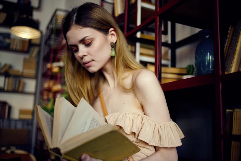 Женщина с книгой в руках читает в библиотеке и отдыхает в кафе