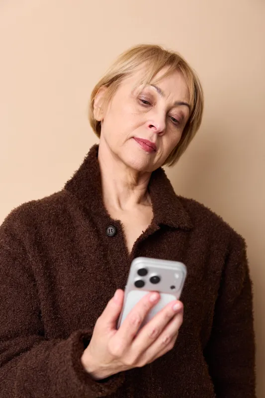 Elderly woman looks stressed with anxiety, holding a smartphone indoors. Concern and loneliness show on her face, suggesting mental health worries today.