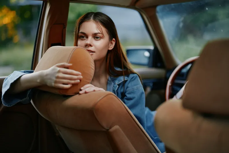 Young woman enjoying a carefree moment inside a vintage car, exuding relaxation and joy with her casual denim attire.