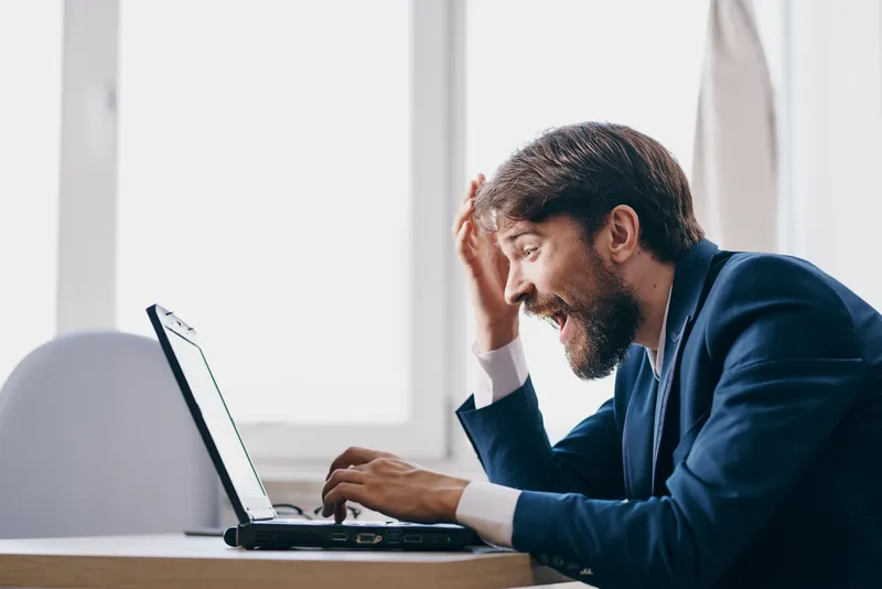 Менеджер работает за ноутбуком в офисе, испытывая эмоции, связанные с интернетом и профессиональной деятельностью