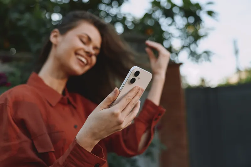 Young woman enjoys outdoor lifestyle as she takes a selfie with a smartphone, smiling, wearing a red shirt, casual look, natural light, candid moment in daylight