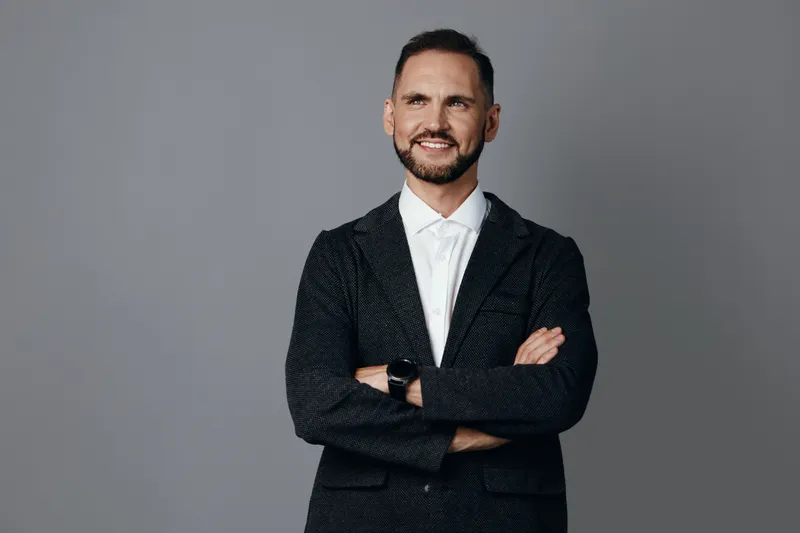 Professional businessman stands against a solid colored background with arms crossed, exuding confidence, leadership, and a friendly approach suitable for corporate media.