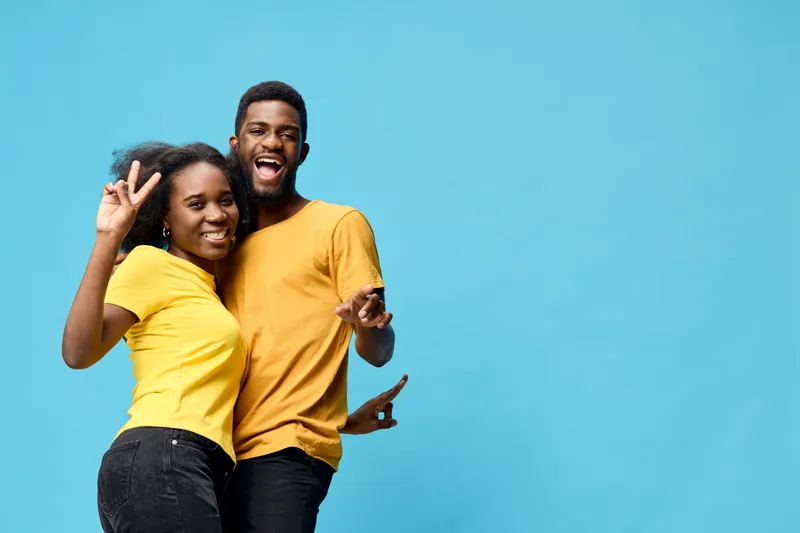 Cheerful young African American couple in matching yellow t shirts posing against a bright blue background, expressing joy and positivity together