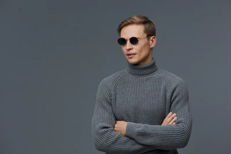 thoughtful young caucasian man wear sunglasses gray sweater crossed arms look aside isolated on gray background digital detox mental health concept