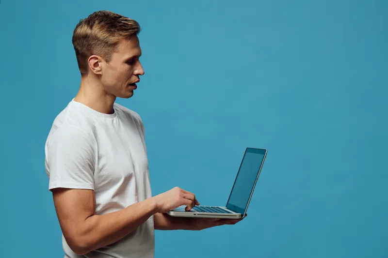 young caucasian man working remotely with laptop on blue background casual wear focused digital nomad concept