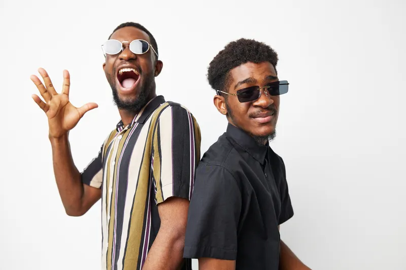 Two smiling African American men wearing trendy sunglasses, showcasing joy and friendship in a vibrant setting. Perfect for capturing moments of carefree youthfulness.