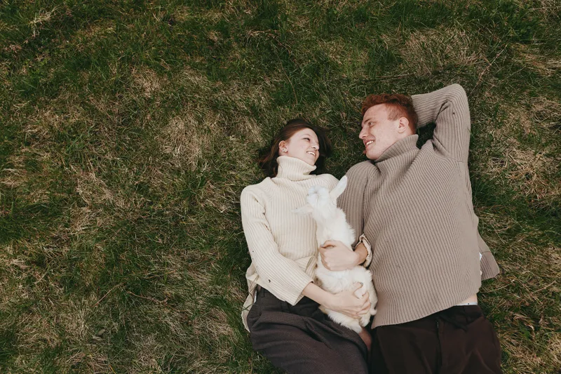Happy couple outdoors goat kid lifestyle romance sweater grass smile cuddle, casual peaceful nature outdoor bonding, joyful moment in relaxed scene with warmth