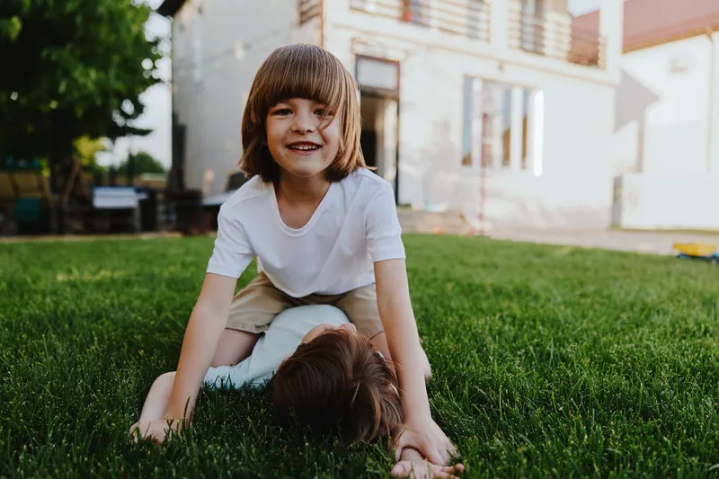 Happy boy playing outdoors with his sibling, enjoying time in the sunny garden. Laughter and excitement fill the air, creating a joyful atmosphere.