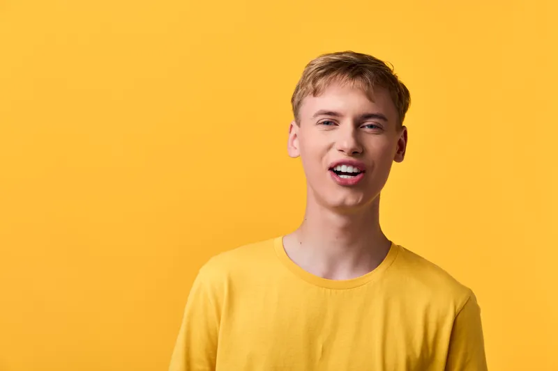 Young man wearing a yellow shirt stands against a vivid yellow background, creating a bright, energetic fashion look suitable for lifestyle and casual style shoots