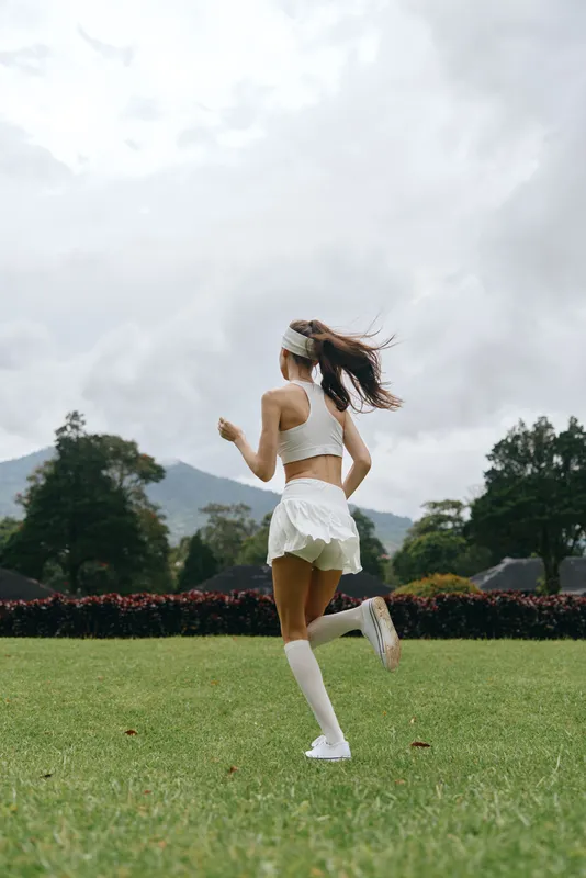 Young athletic woman running in a white sports outfit on a green field, conveying energy and freedom in nature