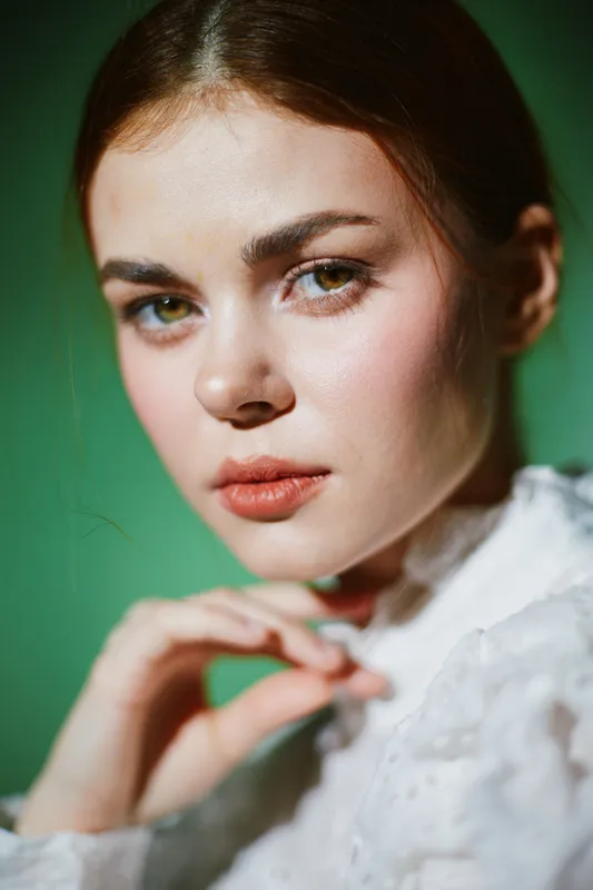 Close up portrait of a young woman with fair skin and green eyes, showcasing natural beauty against a soft green background, evoking elegance and serenity