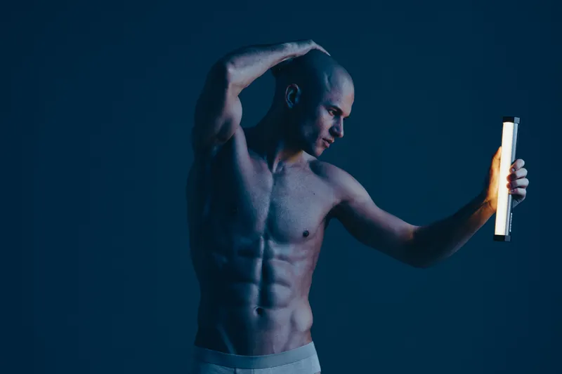 Athletic man posing dramatically with a light, showcasing his physique against a dark background. The composition emphasizes strength and creativity in a low-key setting.