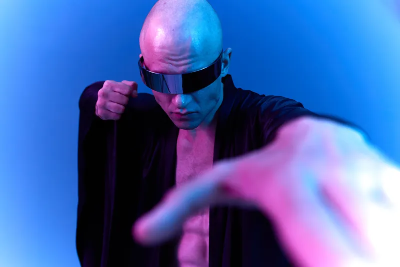 Bold man with futuristic sunglasses striking a powerful pose, surrounded by vibrant blue hues. The dynamic composition reflects strength and confidence, capturing a unique style.