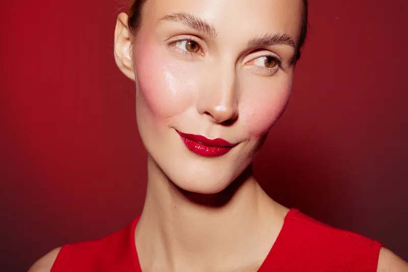 Close-up of a smiling woman with glossy red lips and natural skin wearing a red top against a red background. Concept of beauty, makeup, skincare, and fashion portrait.