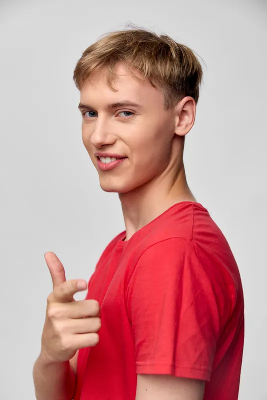 Young man in a red t shirt points at the camera with a confident smile, casual studio shot featuring a friendly gesture, clean background, suitable for lifestyle, advertising or product campaigns
