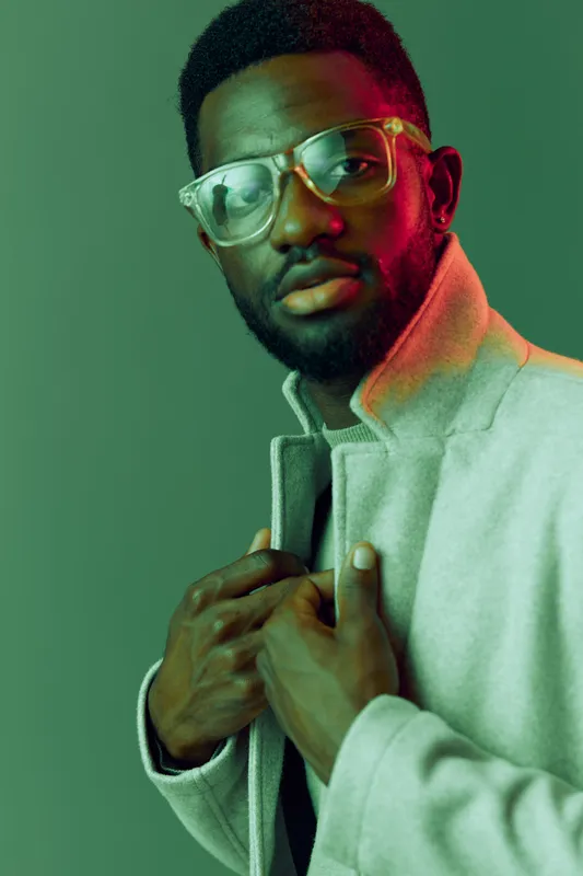 Stylish African man wearing glasses and a light coat, expressing confidence with a vibrant green background, ideal for fashion and lifestyle themes