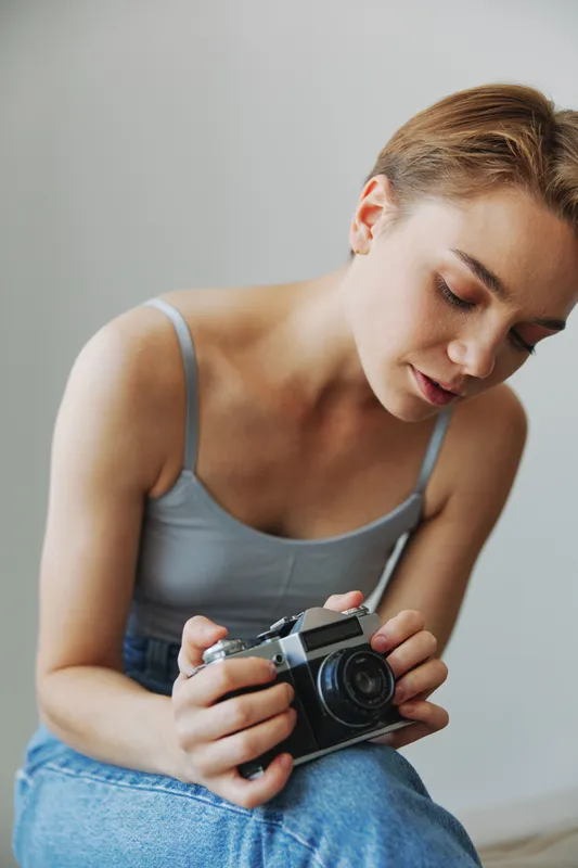 Женщина-фотограф снимает дома на диване на старый плёночный фотоаппарат в студийной обстановке
