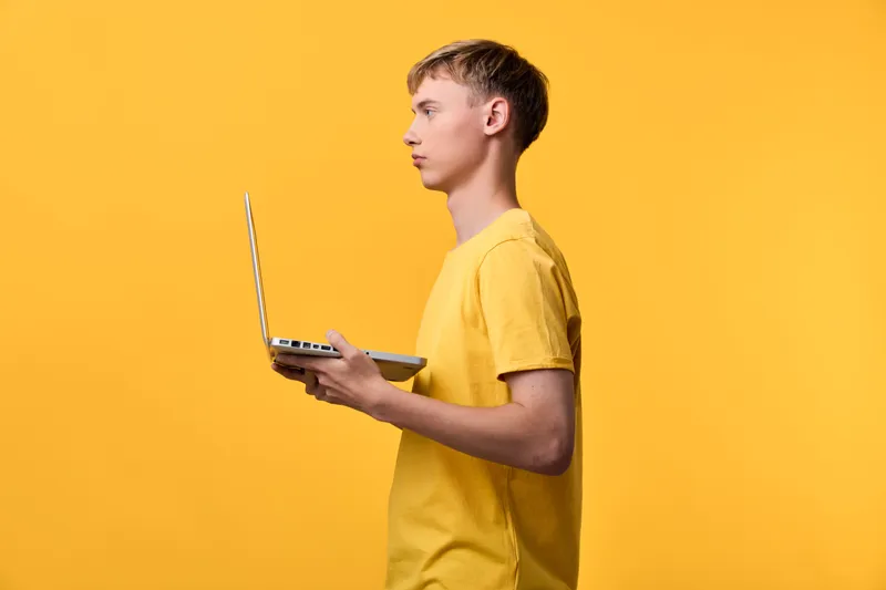 Laptop held by a standing man in a yellow shirt against a vivid backdrop, showcasing modern technology, work focus, and portable device use in a contemporary setting.